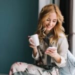 pretty blonde girl sitting window sill with cup