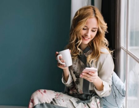 pretty blonde girl sitting window sill with cup